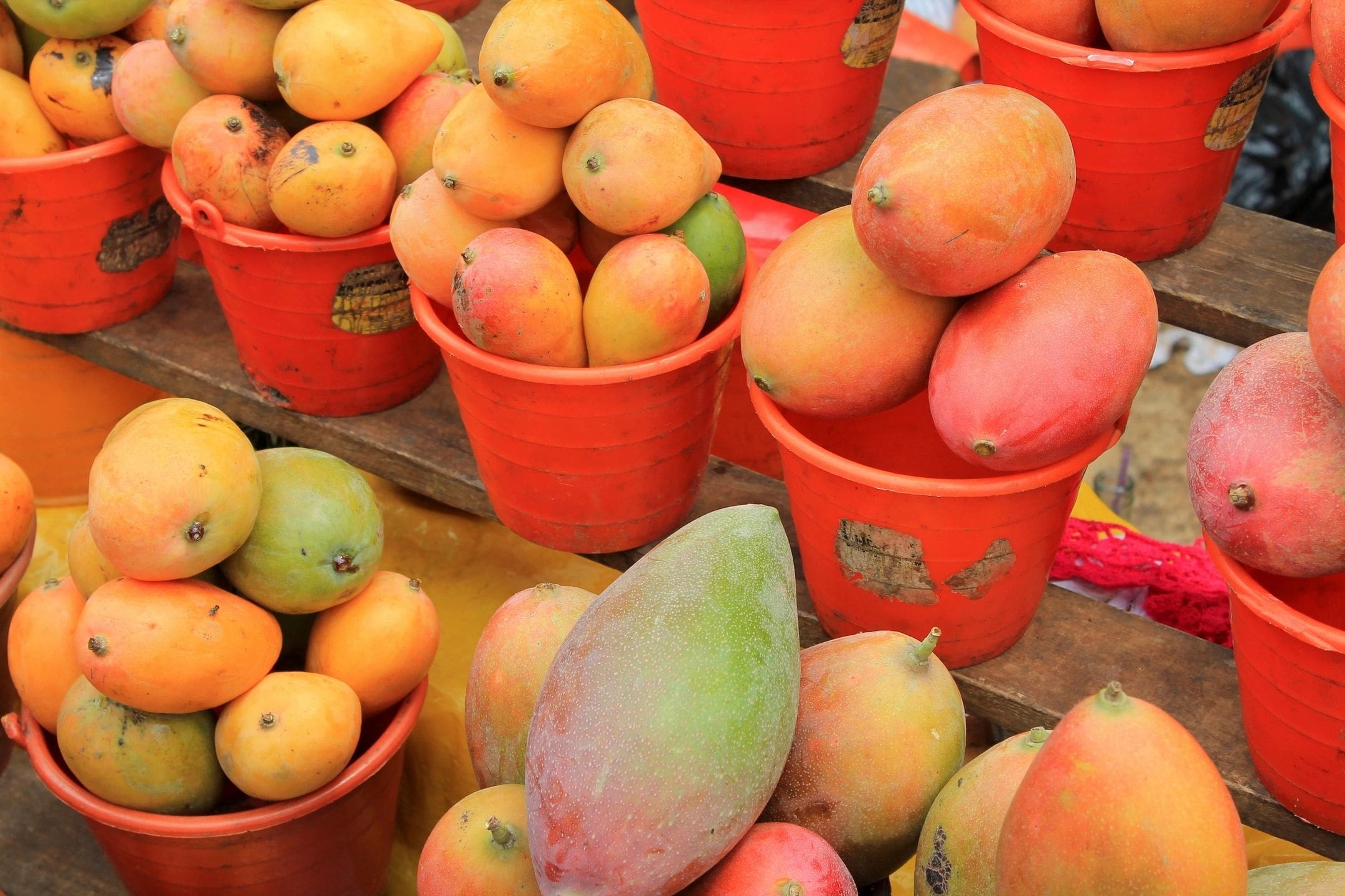 A table filled with lots of fruit in red buckets.