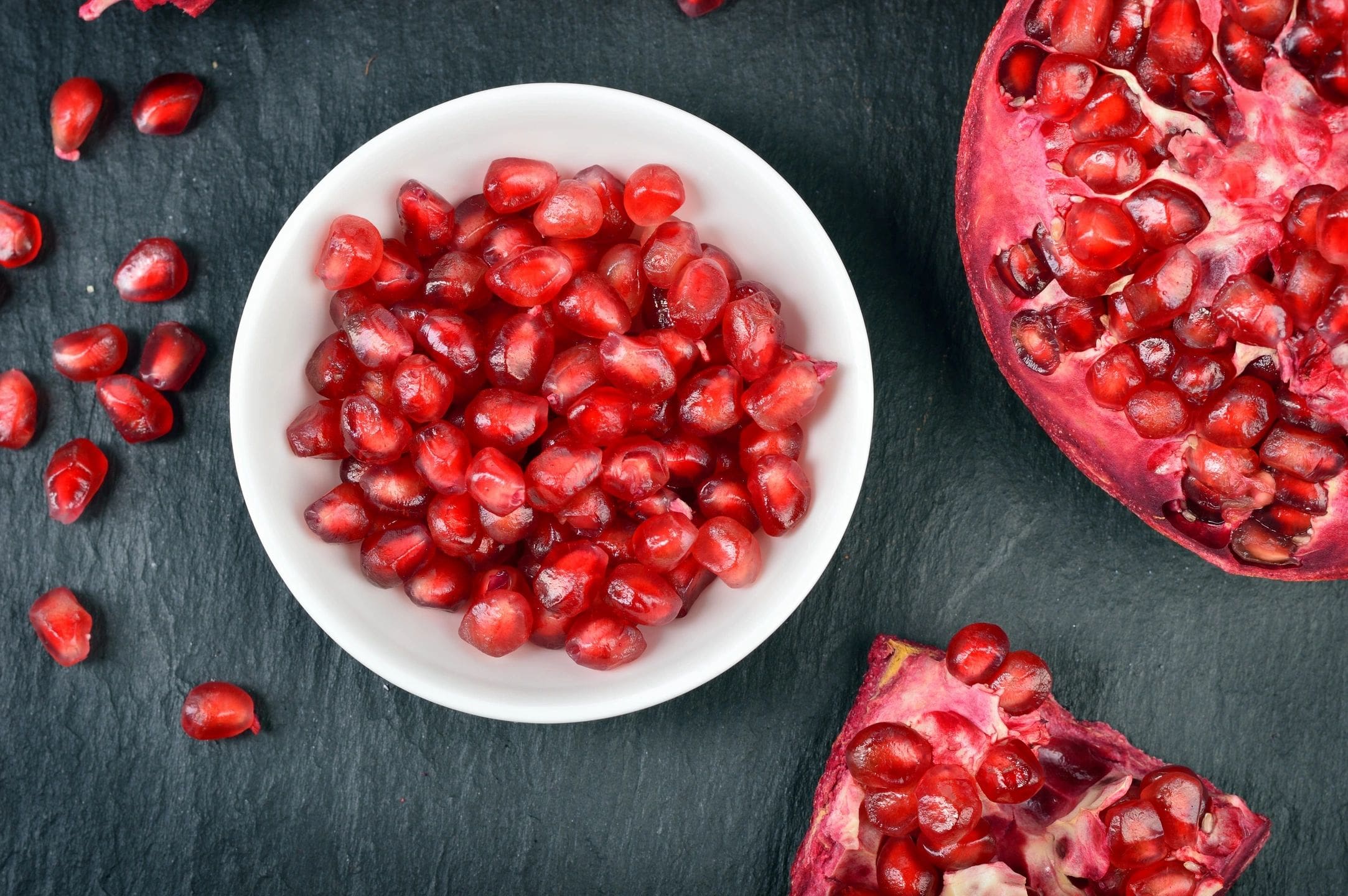 A bowl of pomegranate seeds next to two pieces of fruit.